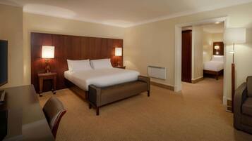 Habitación de hotel con una cama grande, dos mesitas de noche con lámparas, un escritorio con una silla y un pequeño banco.