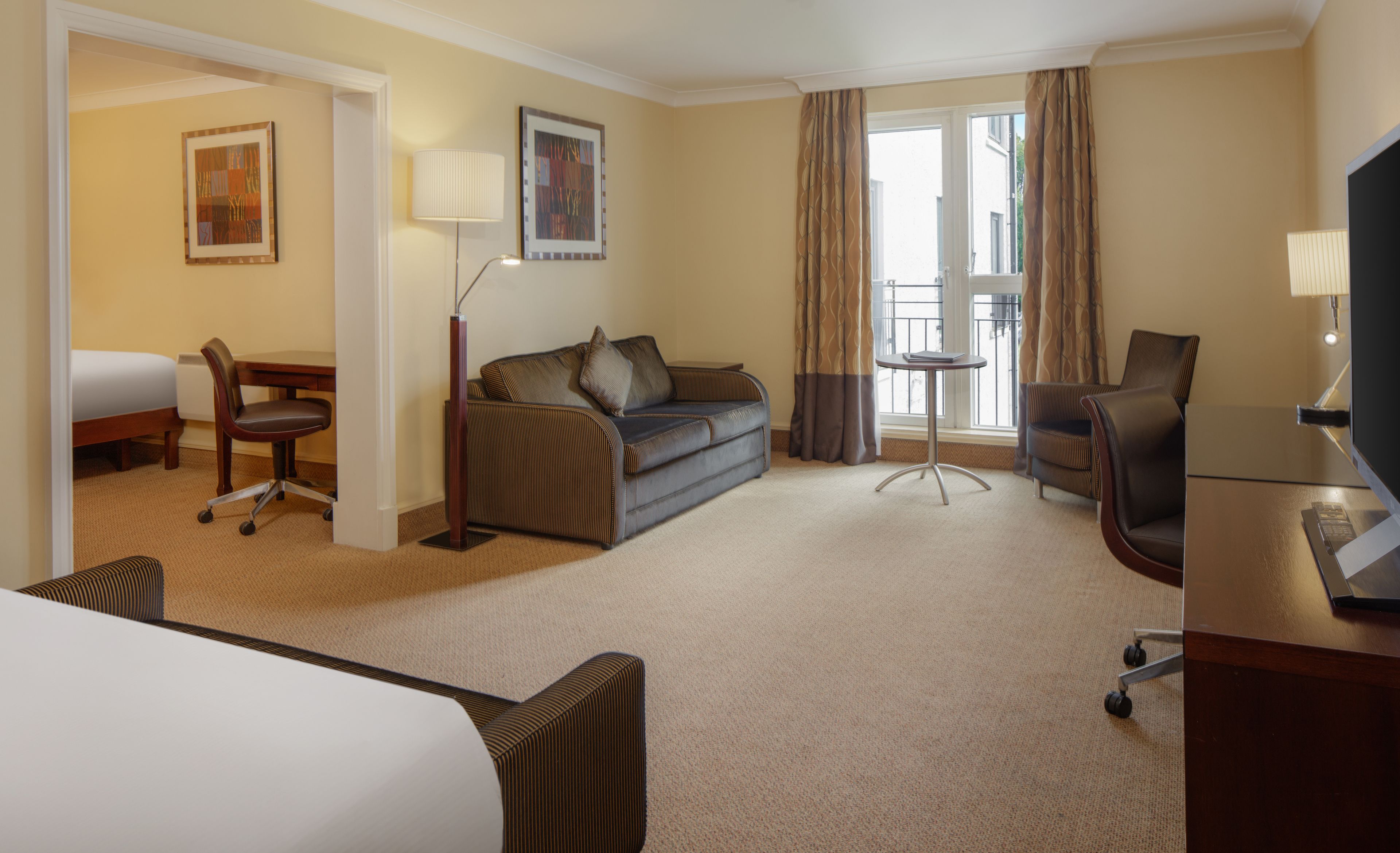 Habitación de hotel con cama, sofá, escritorio, silla, lámpara y televisor.