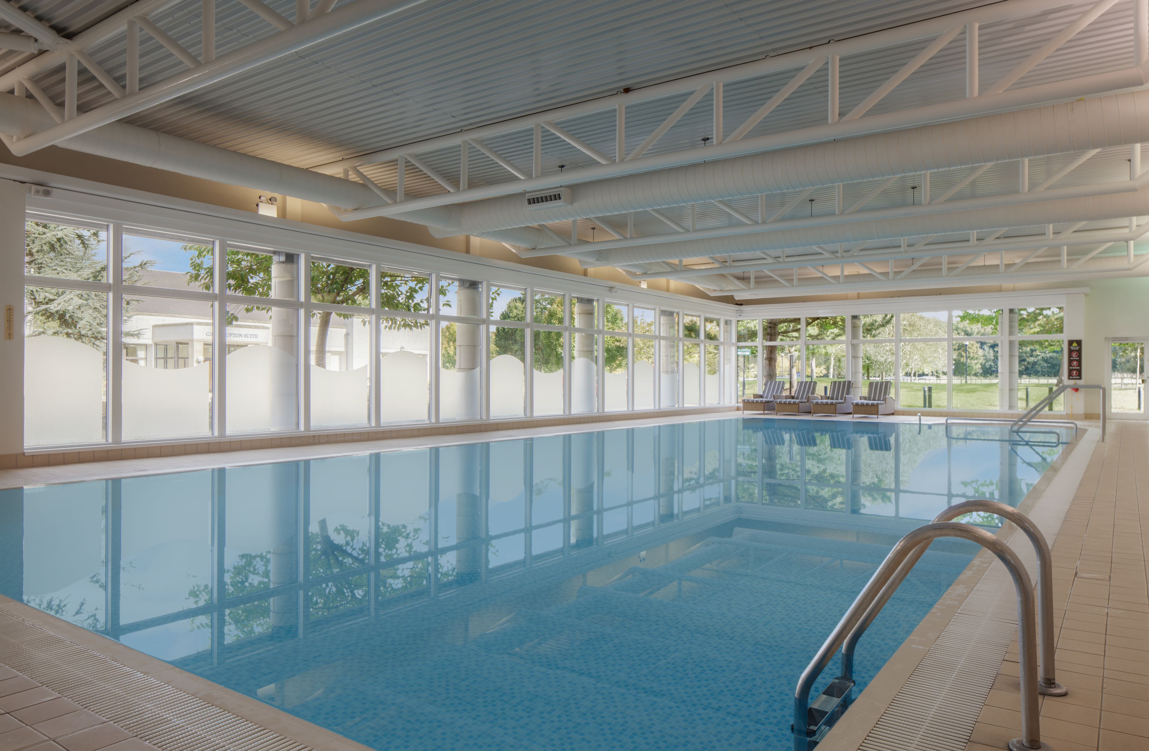 An indoor swimming pool with clear glass walls, a tiled floor, and a metal ladder.
