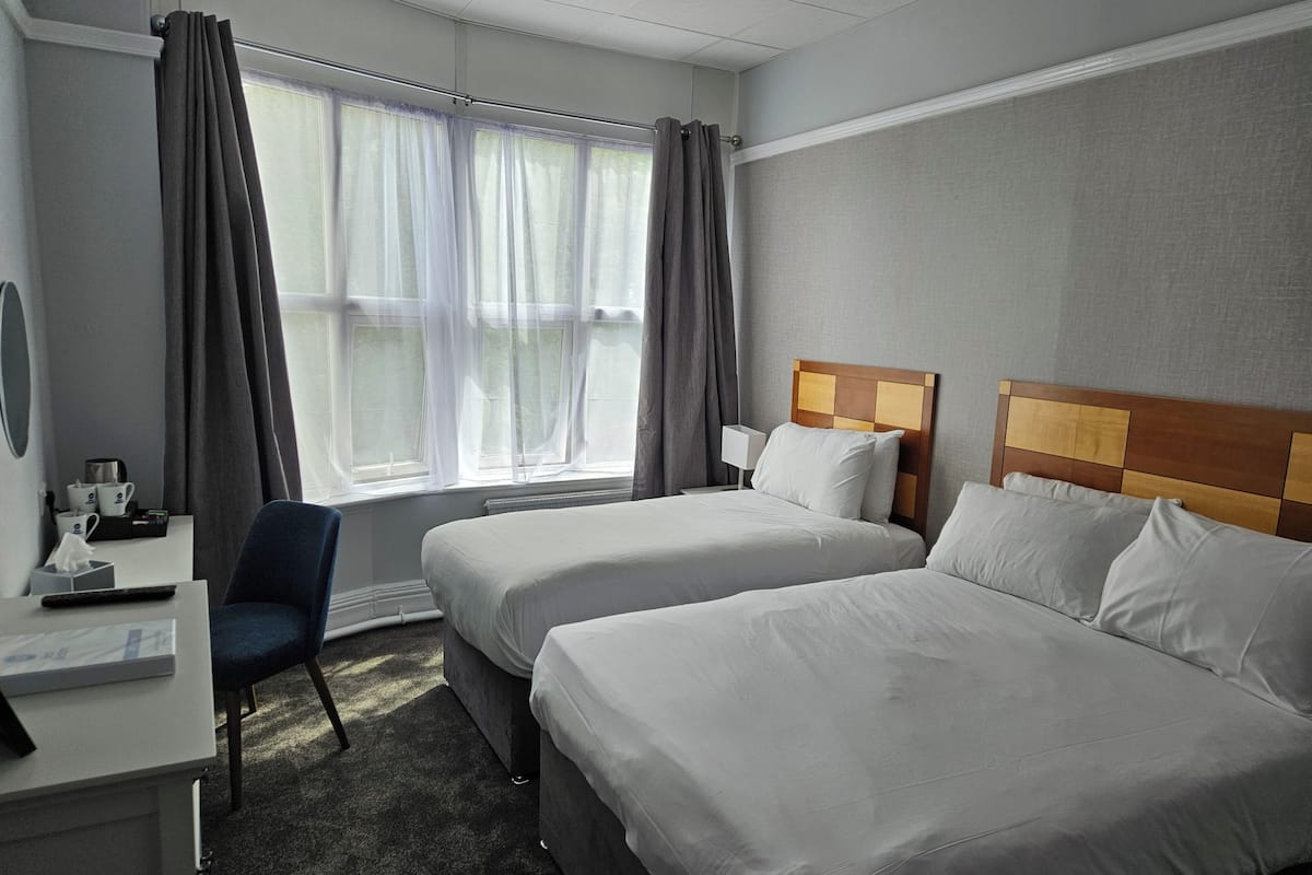 Hotellihuone, jossa on kaksi sänkyä, työpöytä, tuoli, ikkuna verhoilla ja yöpöytälamppu.