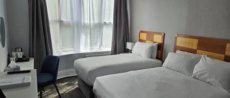 Habitación de hotel con dos camas, un escritorio, una silla, una ventana con cortinas y una lámpara de noche.