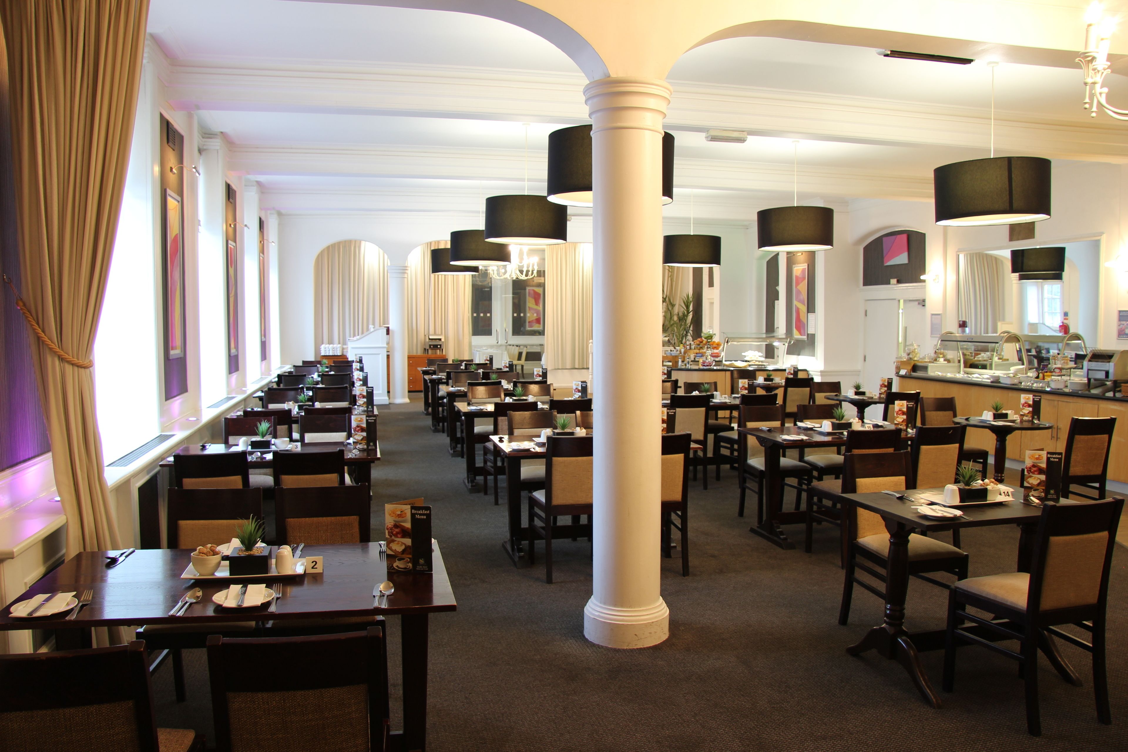 Ein geräumiges Restaurant mit mehreren Tischen und Stühlen, großen Säulen und Pendelleuchten.