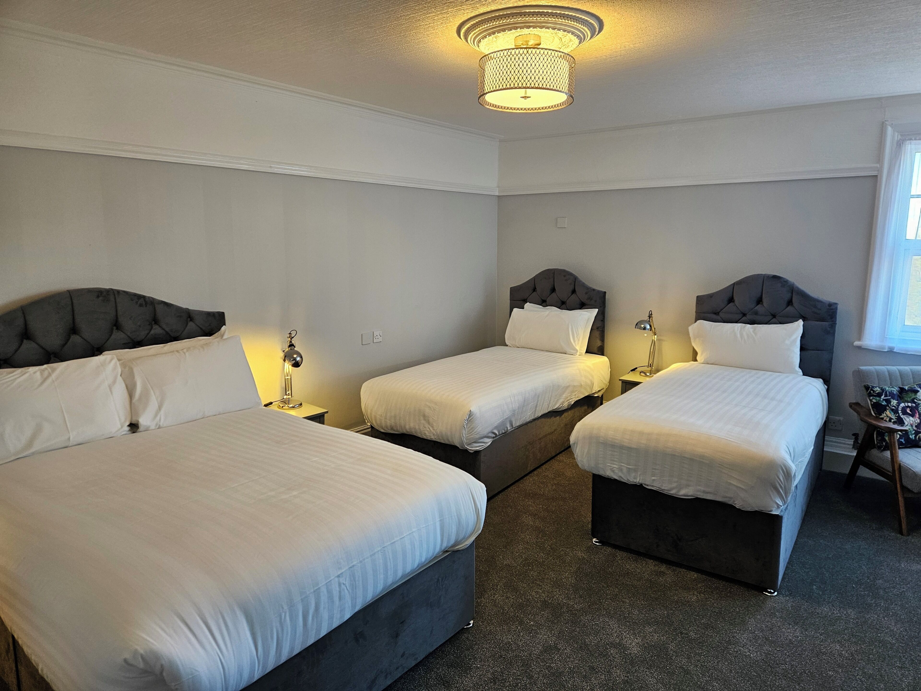 A hotel room with three beds, a desk, and a chair.
