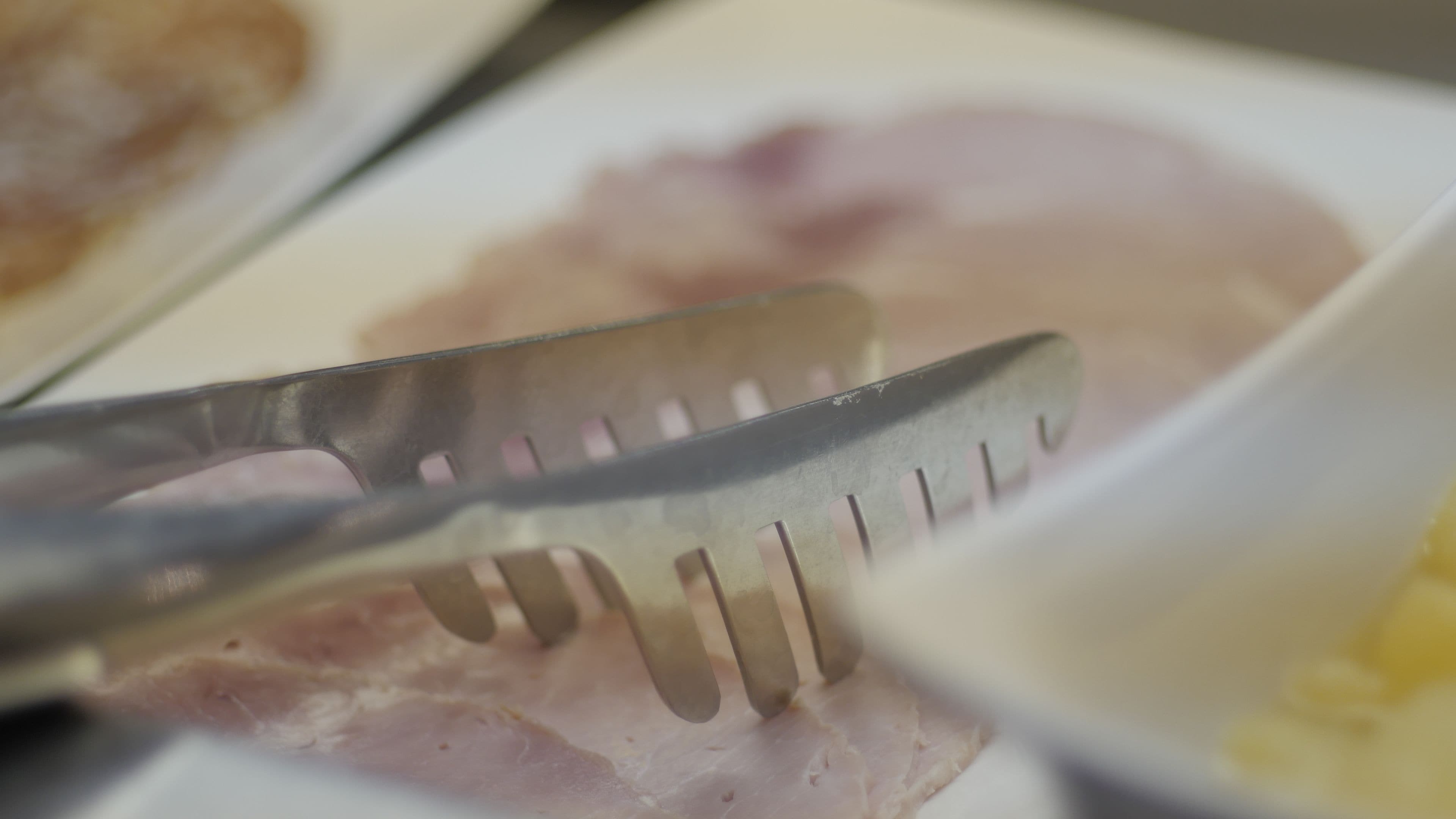 Gros plan sur un couteau et une fourchette posés sur une assiette, avec des tranches de jambon et un petit bol contenant un aliment jaune, probablement un accompagnement.