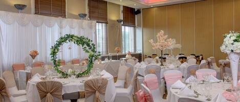 Un salón de banquetes con mesas redondas, sillas blancas y rosas, y centros de mesa florales.