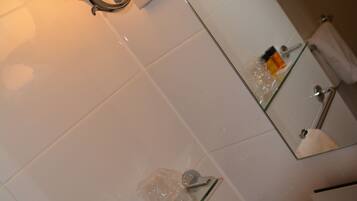 Un baño con repisa de vidrio que sostiene artículos de aseo, un perchero y un espejo con lámpara.