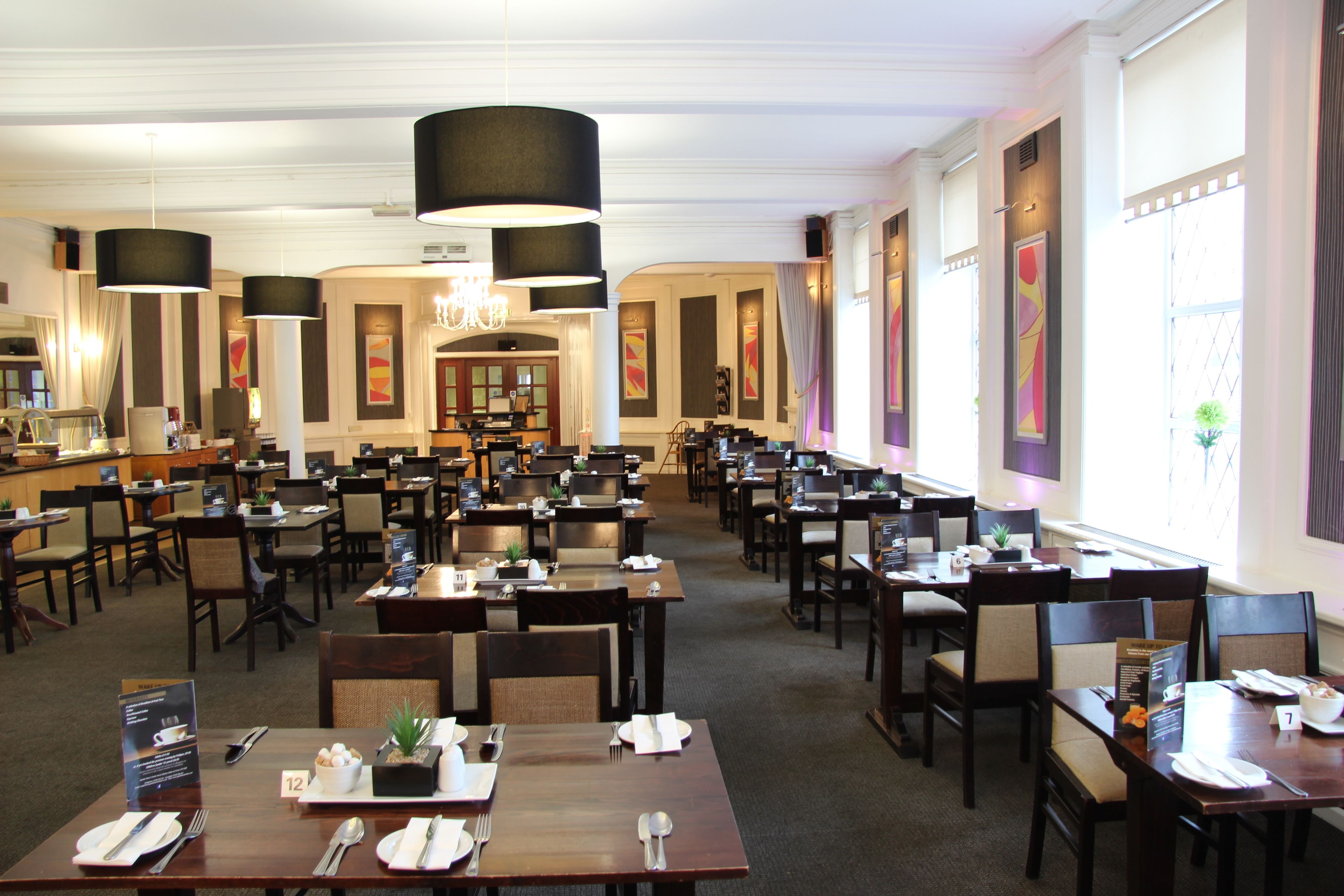 Un'ampia sala da pranzo con diversi tavoli e sedie, grandi lampadari pendenti neri e un lampadario.