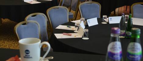 Une salle de conférence avec des tables disposées pour une réunion, équipée de porte-noms, de bouteilles d’eau et d’une tasse à café.