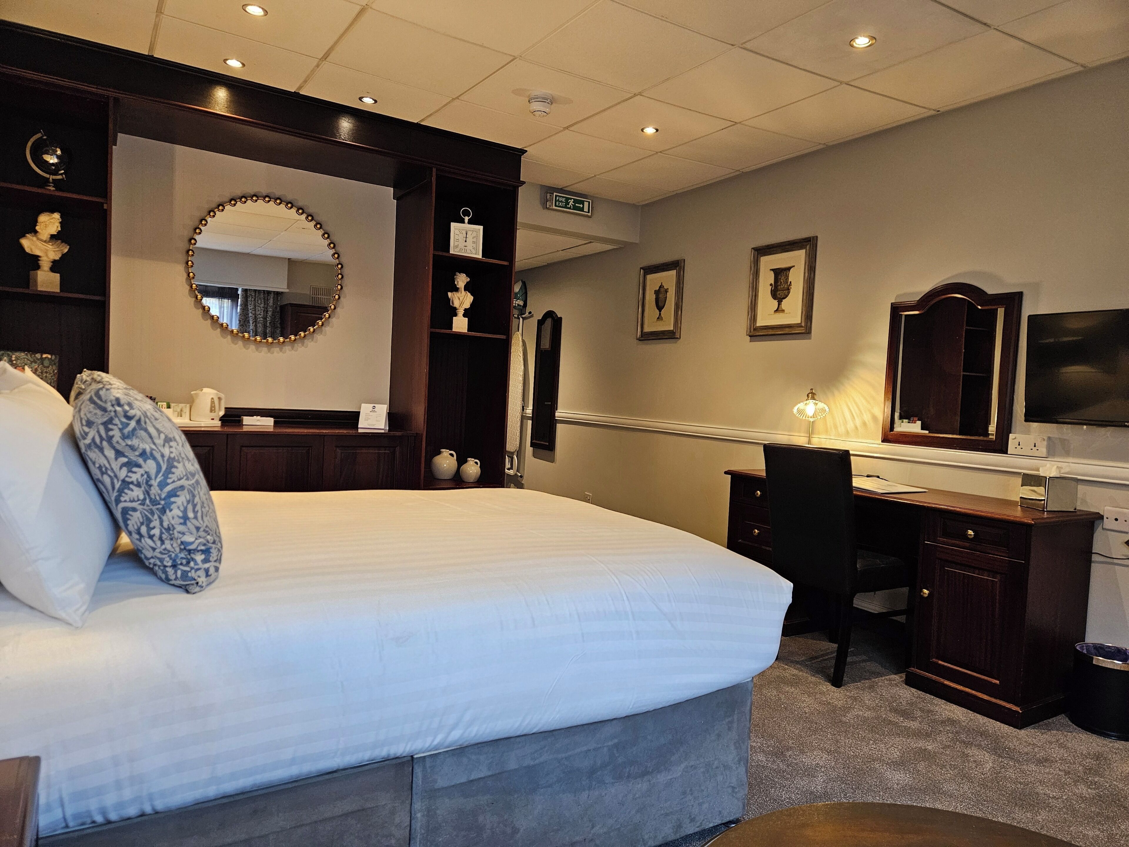 Een hotelkamer met een groot bed, een bureau, een stoel, een spiegel en een televisie.