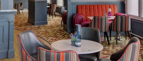Un restaurante acogedor con un asiento tapizado color rojo, sillas a rayas y piso con diseño.
