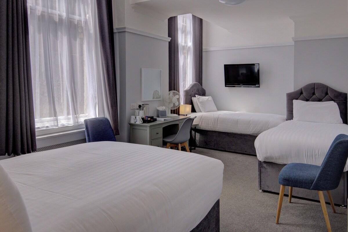 Habitación de hotel con dos camas, un escritorio, una silla, televisión y ventana con cortinas.