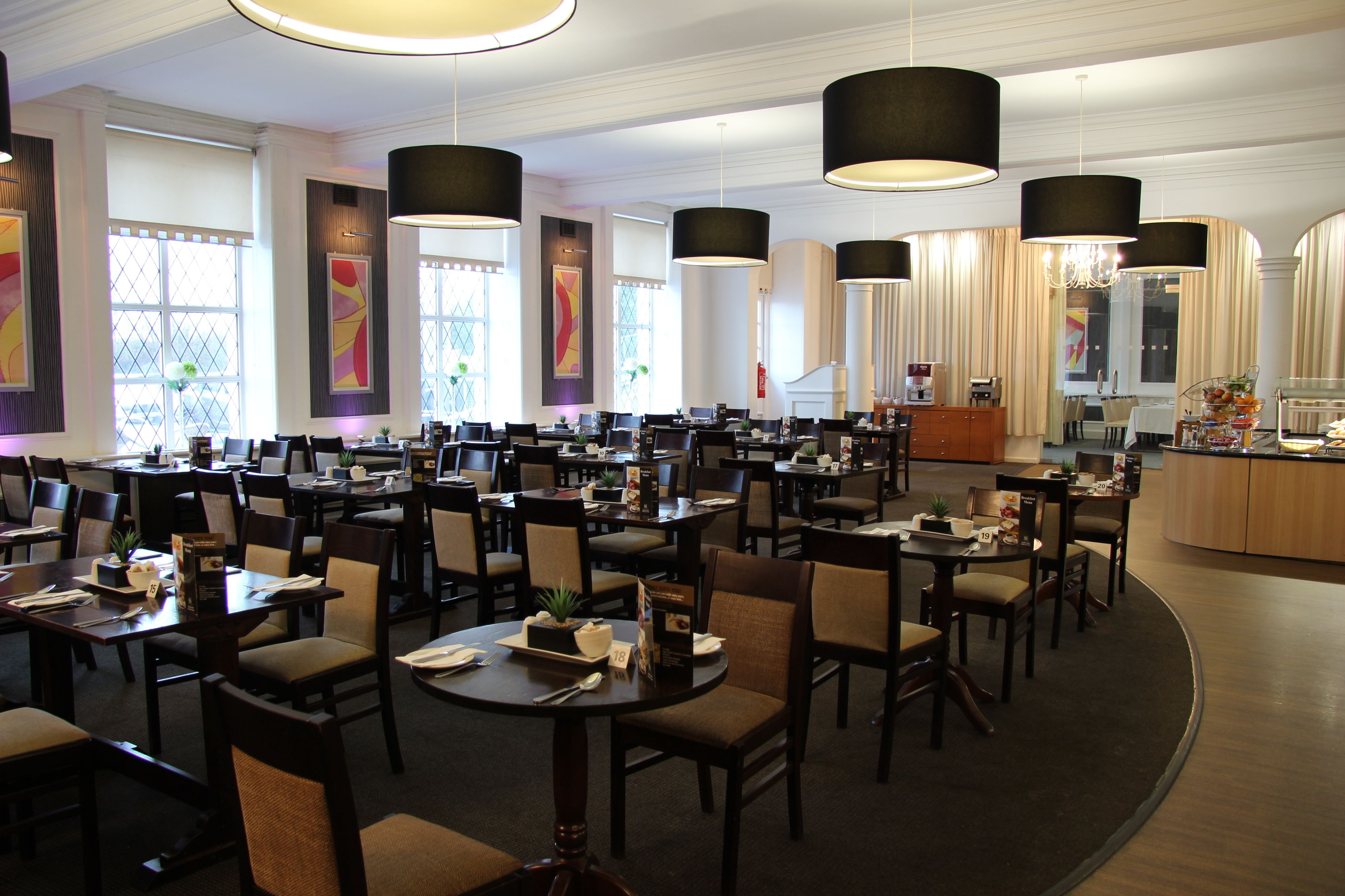 A spacious dining area with multiple tables and chairs, large pendant lights, and a central buffet area.