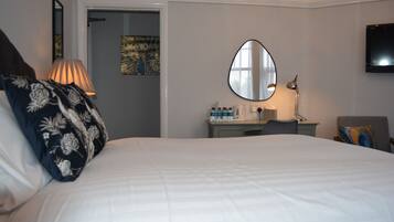 A hotel room with a large bed, a bedside table with a lamp, a mirror, a desk with a chair, and a television on the wall.
