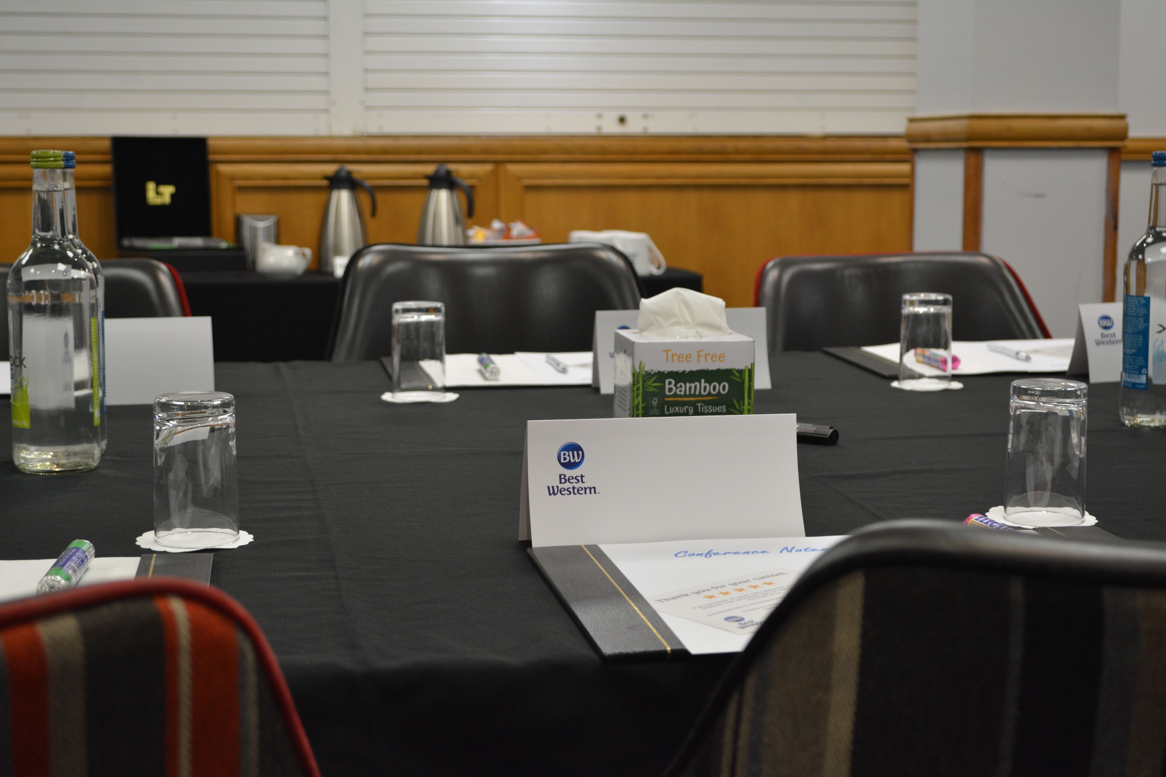 A conference room with a table set for a meeting, including nameplates, water bottles, and a tissue box.