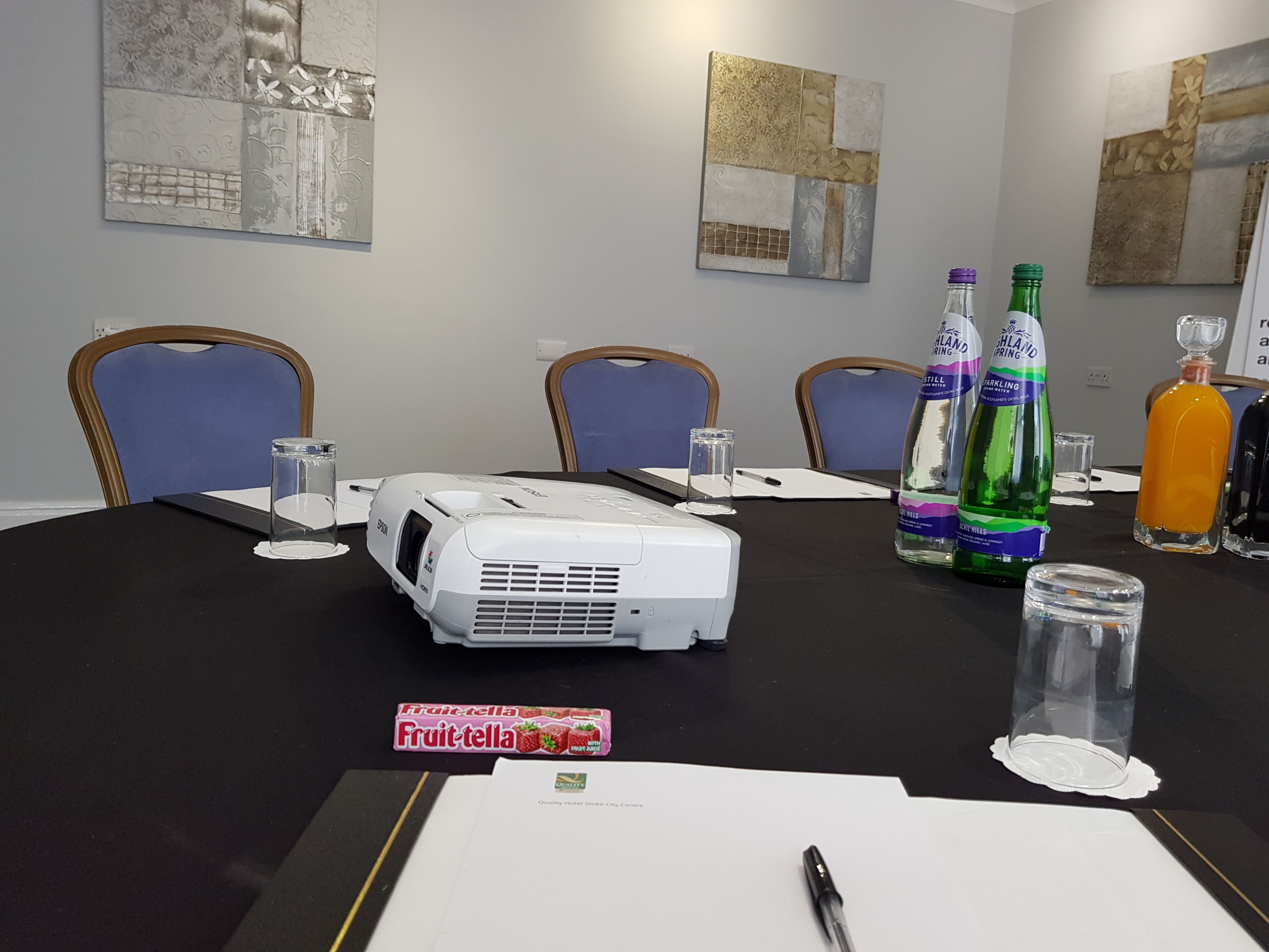 Een vergaderruimte met een beamer, een whiteboard en een tafel met diverse voorwerpen, waaronder flessen en glazen.