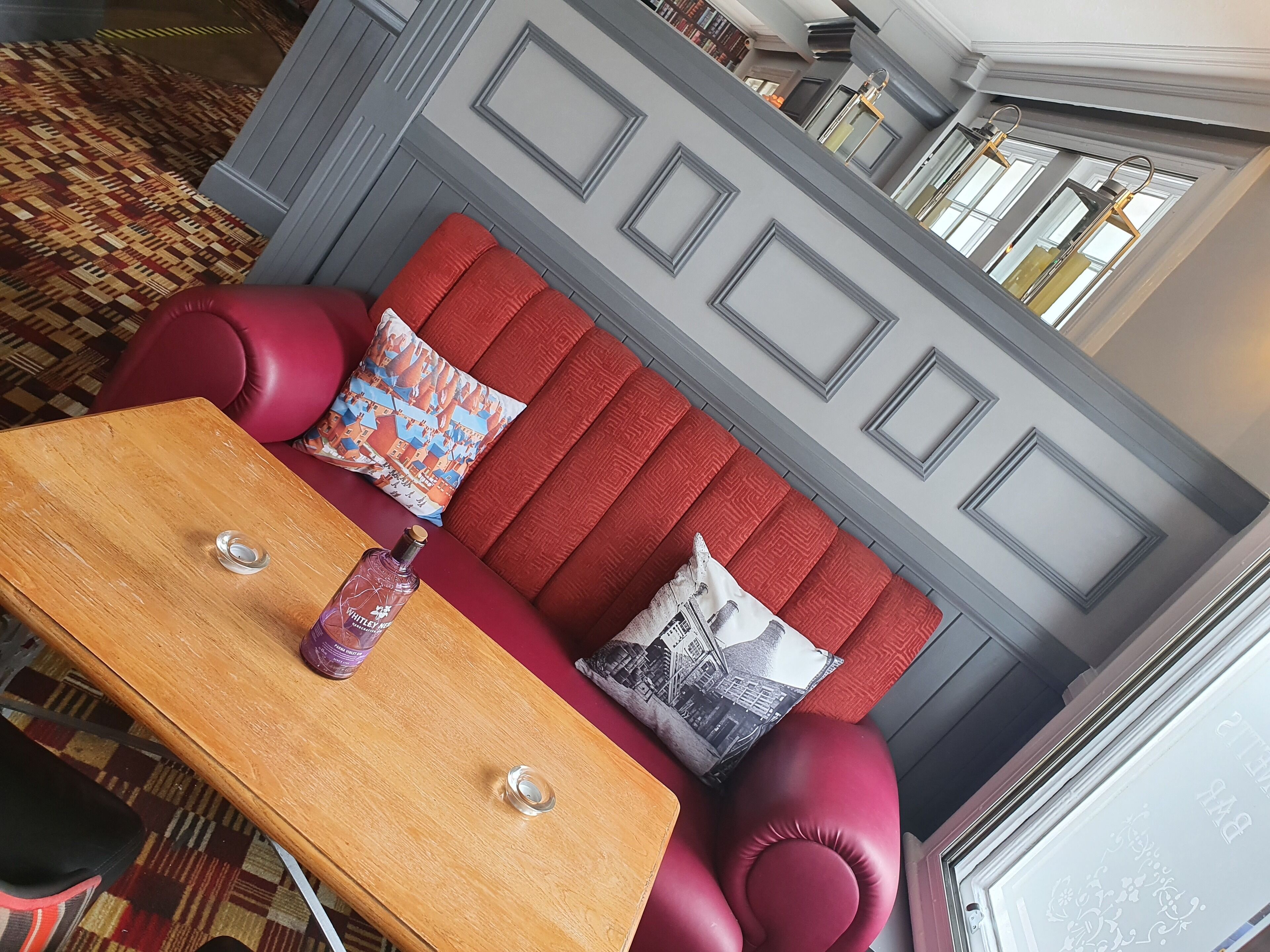 A red sofa with patterned cushions, a wooden table with a bottle, and a patterned rug.