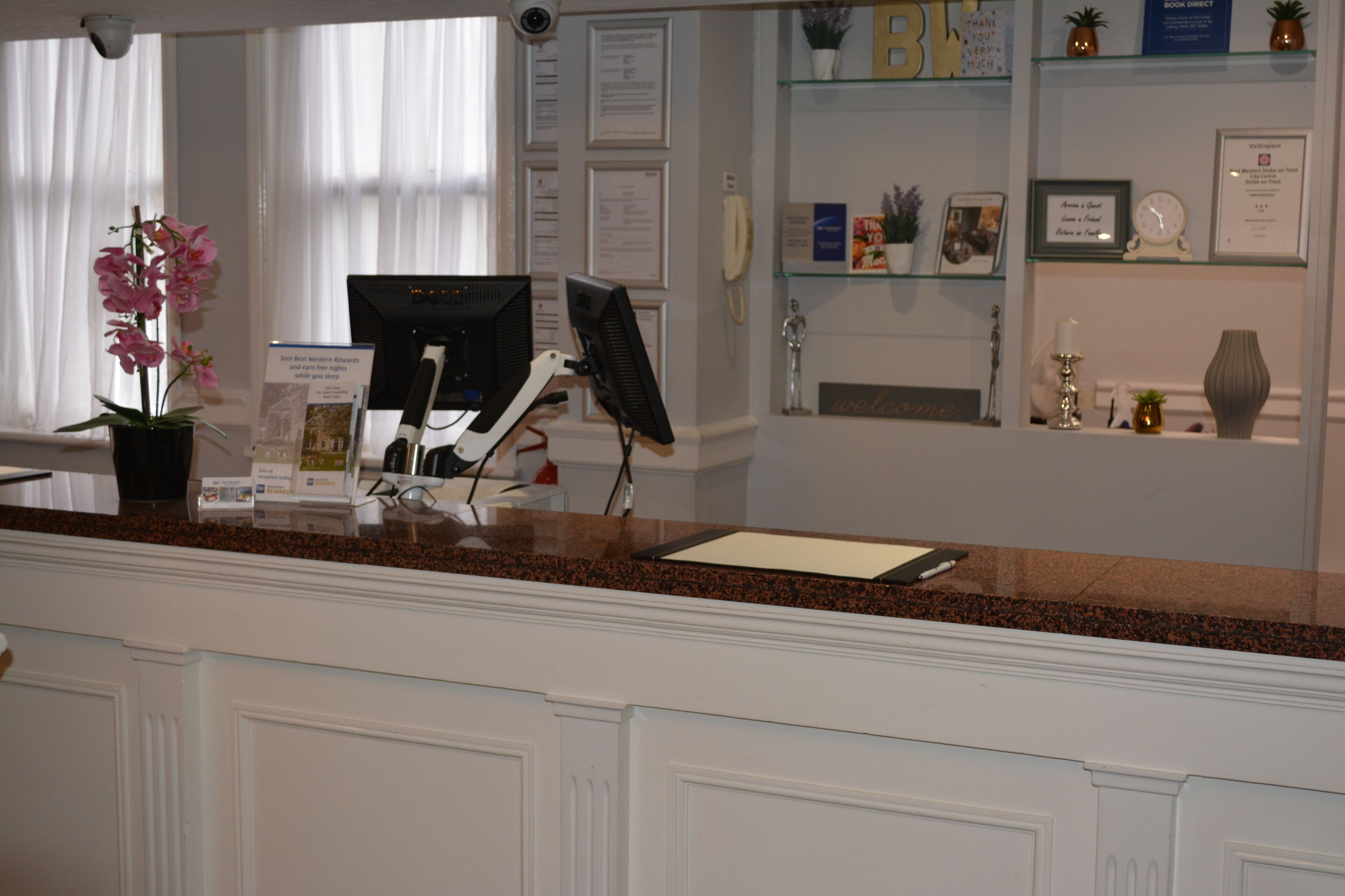 A reception desk with a computer, a potted orchid, and a glass display case with framed items and a clock.