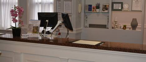 A reception desk with a computer, a potted orchid, and a glass display case with framed items and a clock.