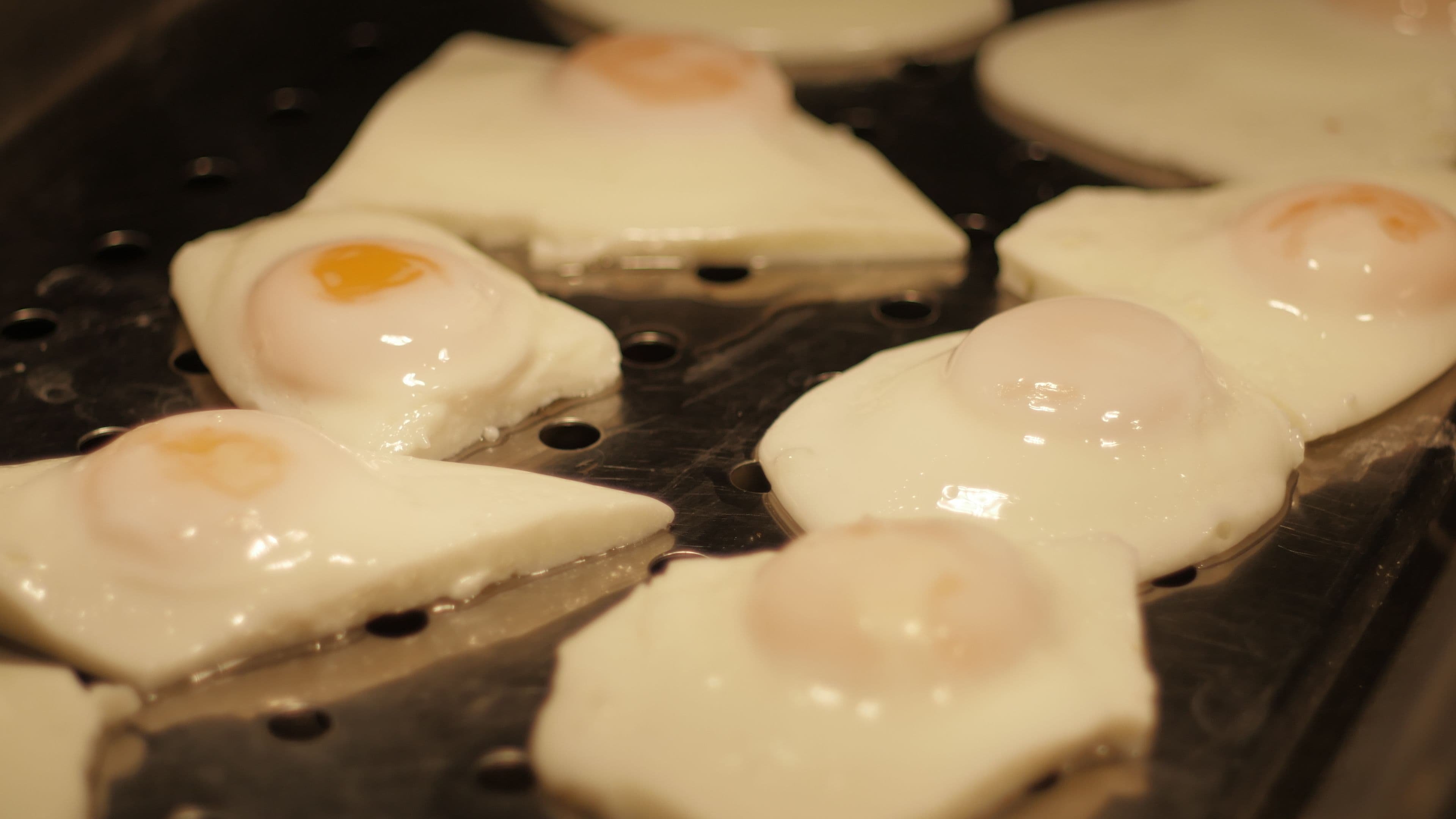 A close-up of a grill with several pieces of food, likely eggs, being cooked.