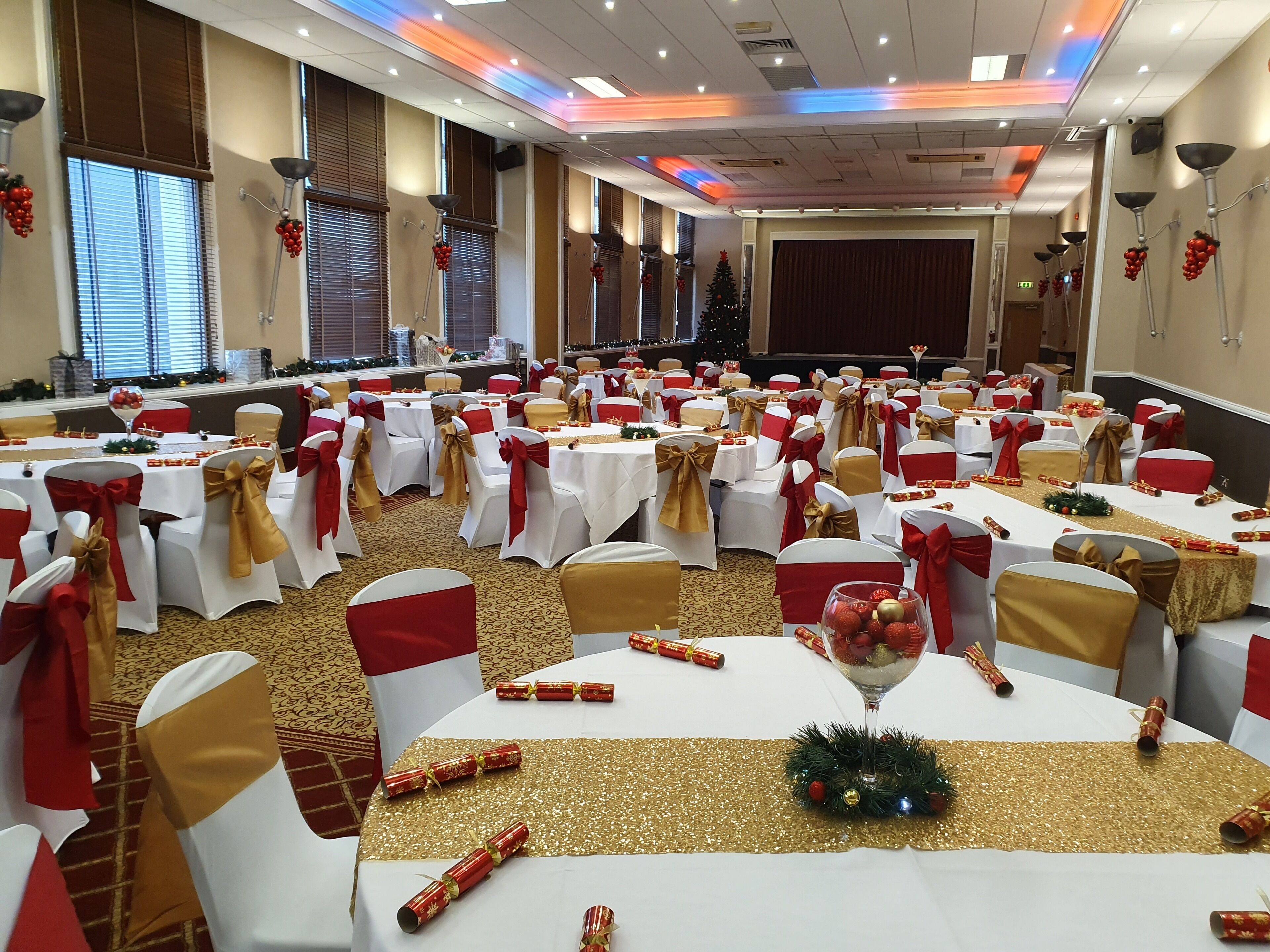 A banquet hall with round tables, white tablecloths, and chairs with red and gold sashes.