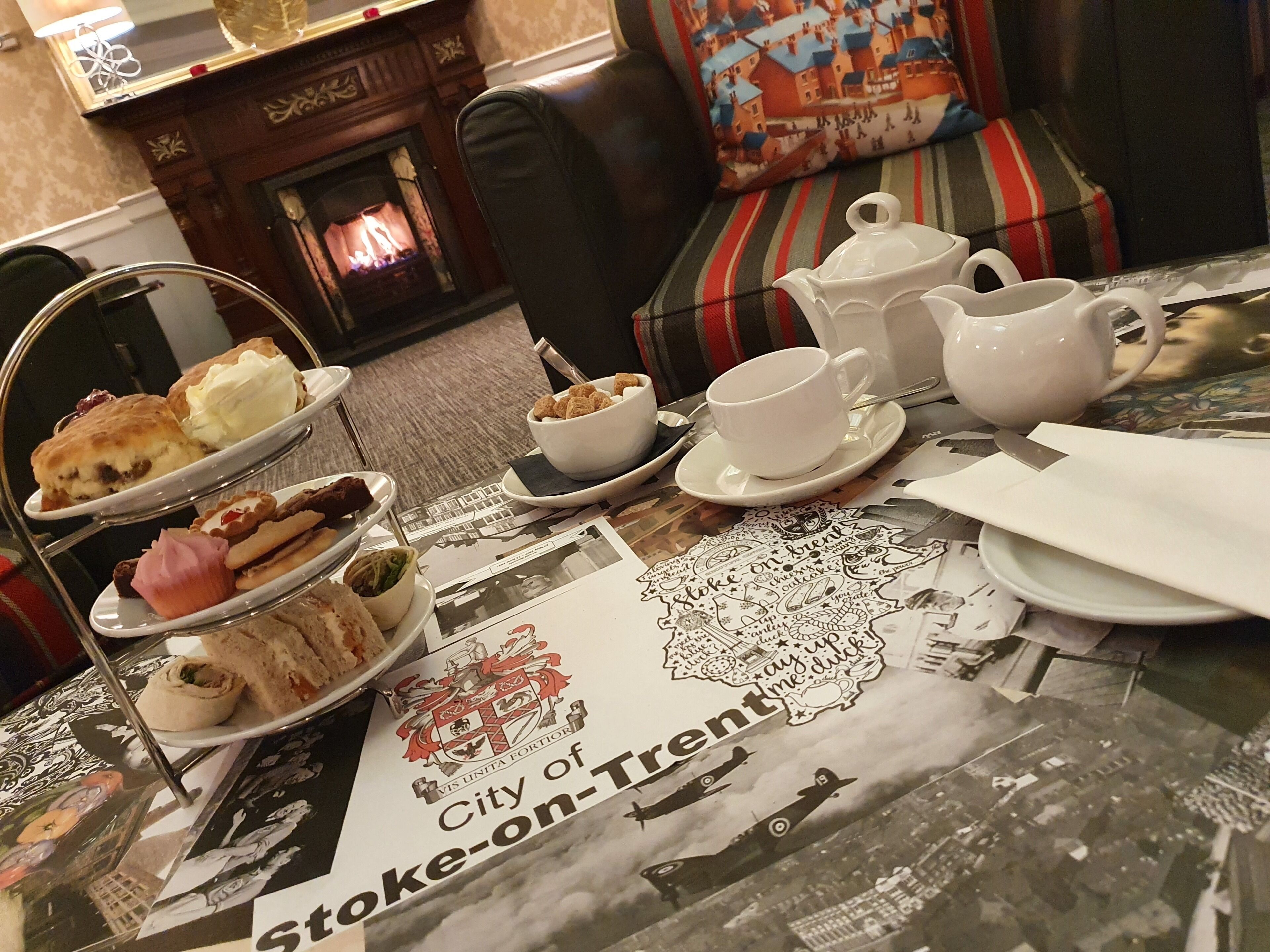 A dining table with a tea set, a menu, and a decorative plate with the City of Stoke-on-Trent emblem.
