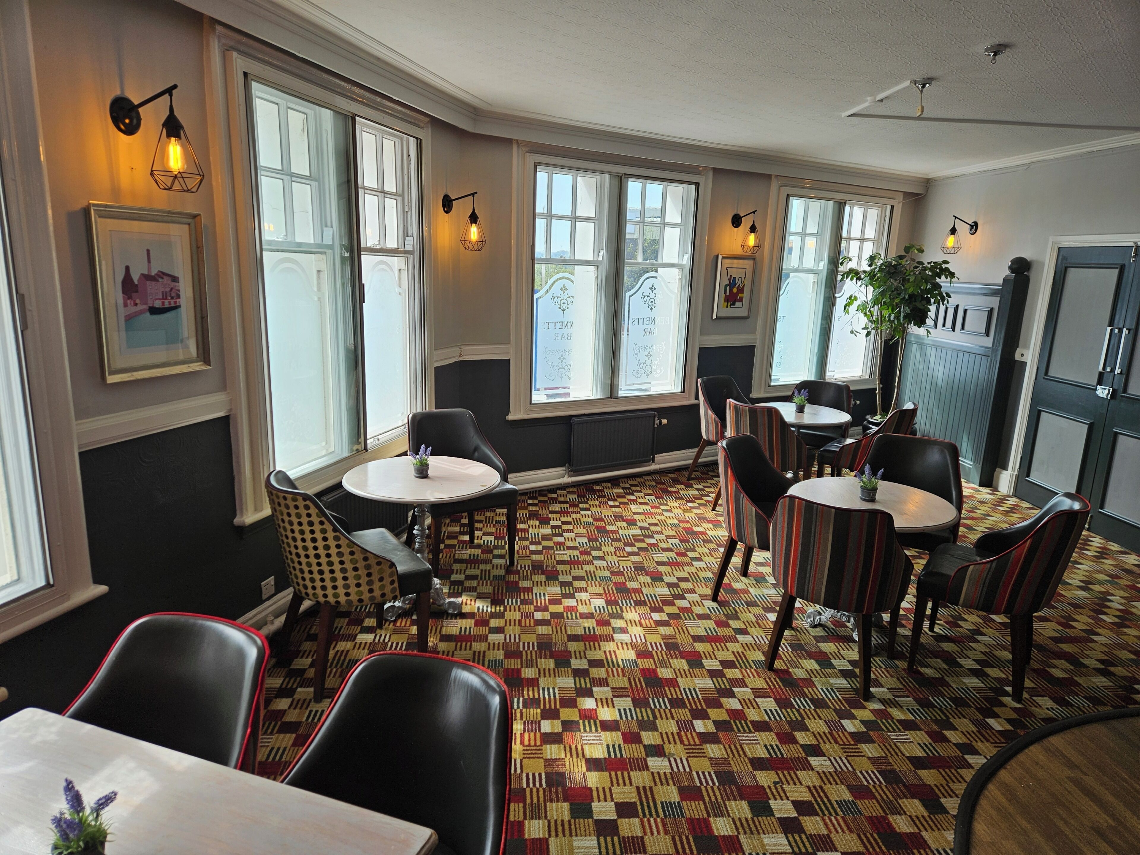 A room with multiple seating areas, large windows, and wall-mounted lighting fixtures.