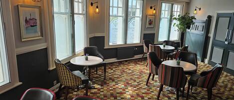 A room with multiple seating areas, large windows, and wall-mounted lighting fixtures.