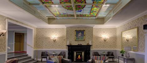 A hotel lounge with a fireplace, comfortable seating, and a decorative ceiling.