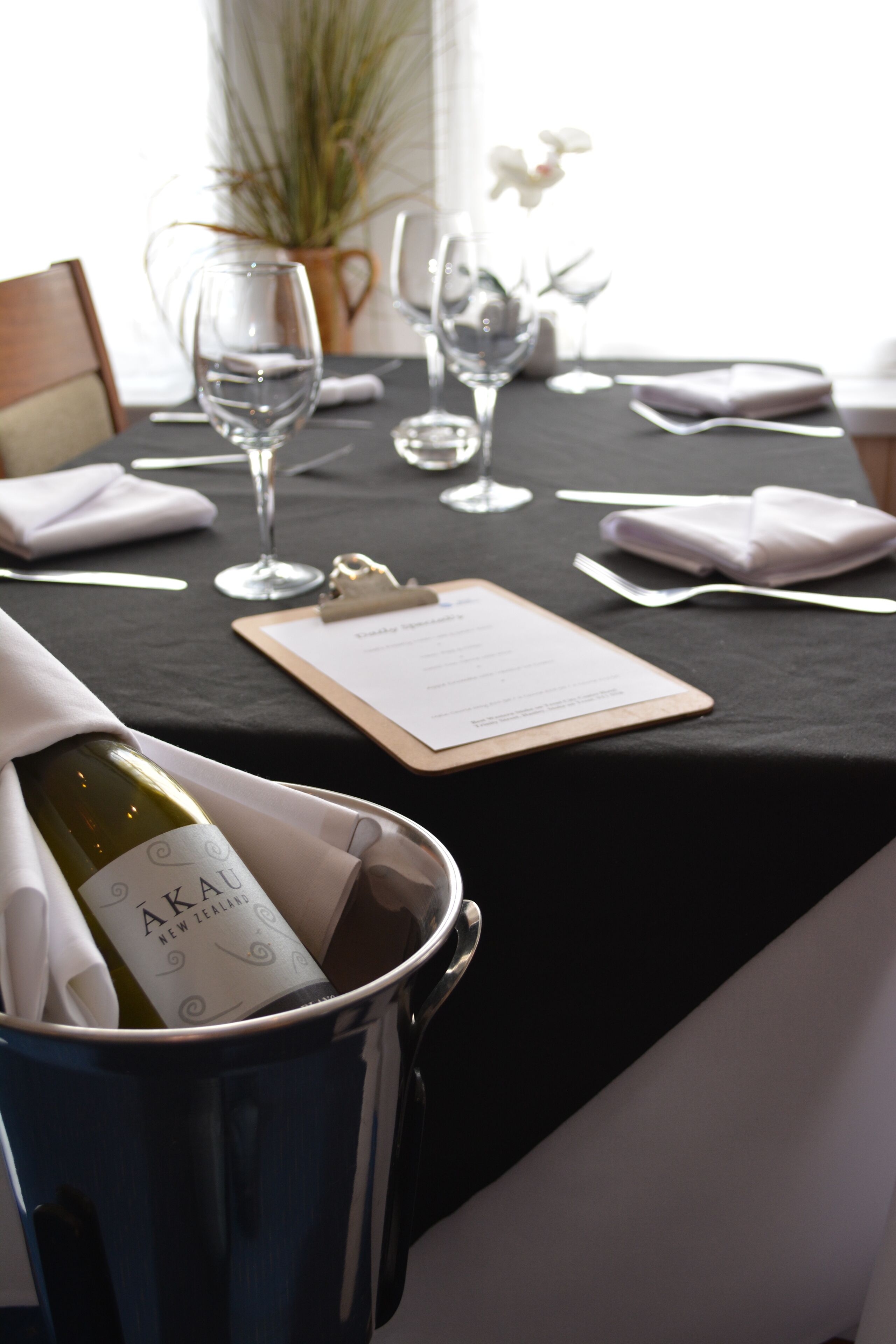 A table set for dining with a bottle of wine, a menu, and a vase of flowers.