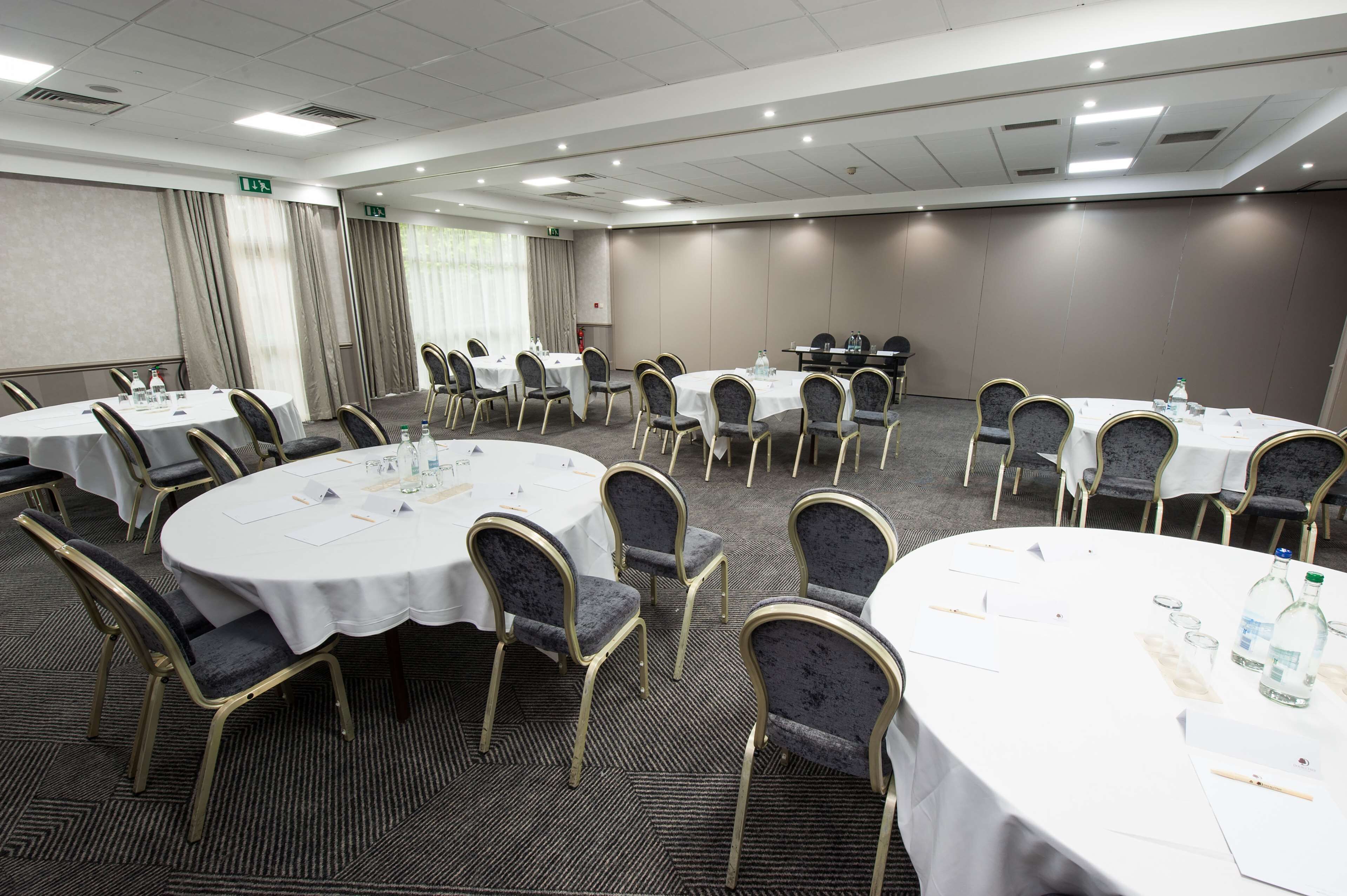 A conference room with multiple round tables, each with white tablecloths and gold chairs.