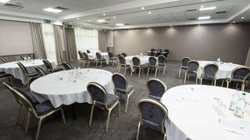 A conference room with multiple round tables, each with white tablecloths and gold chairs.