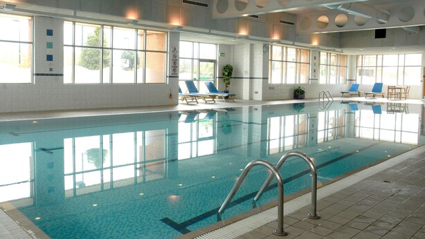 An indoor swimming pool with clear blue water, sunlit windows, and lounge chairs along the sides. - DoubleTree by Hilton Glasgow Strathclyde (Bellshill)