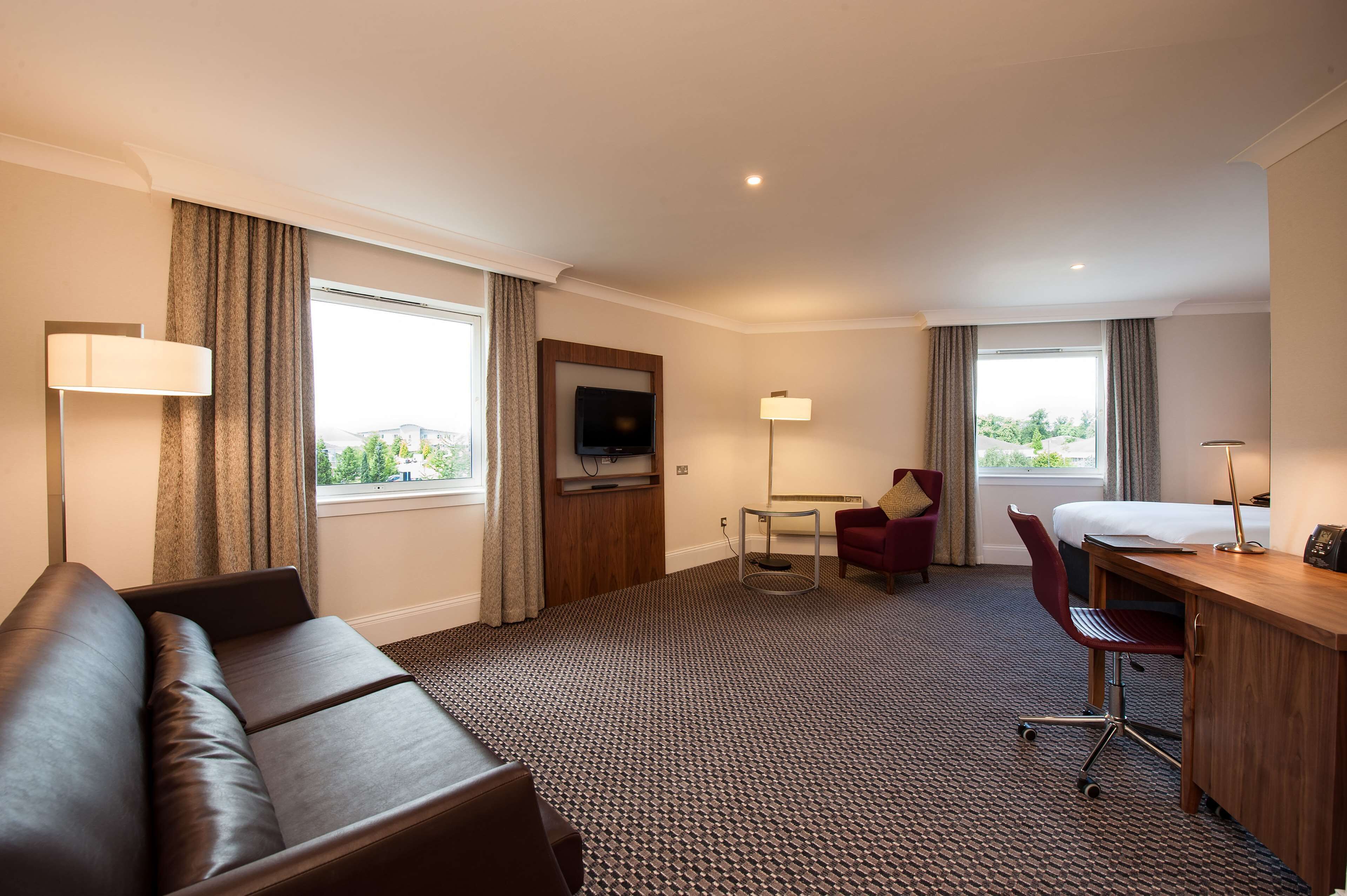 Une chambre d’hôtel équipée d’un canapé, d’un bureau, d’une chaise, d’une télévision et de grandes fenêtres.