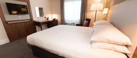 A hotel room with a large bed, a desk, a chair, a TV, and a window with curtains.