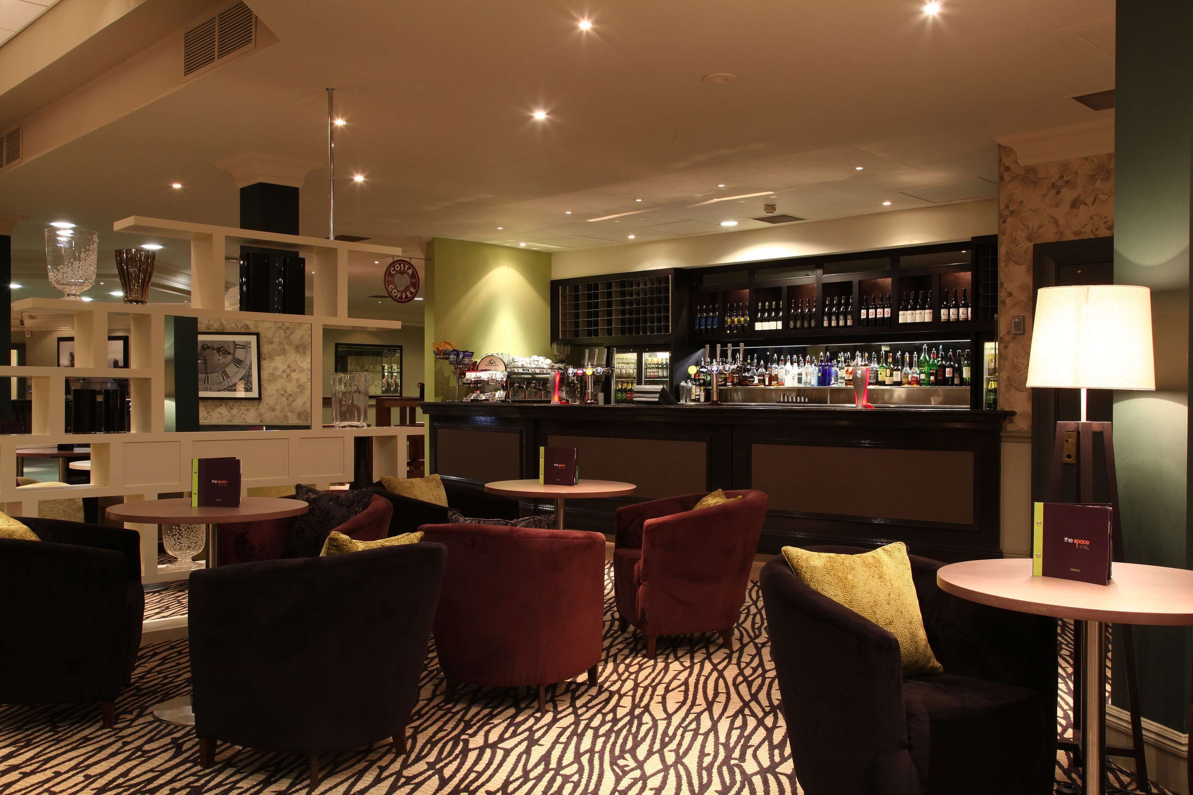 A bar area with seating, shelves with bottles, and a clock on the wall.