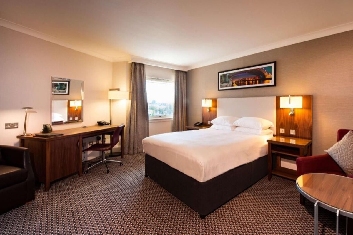 A hotel room with a bed, desk, chair, and a small table.