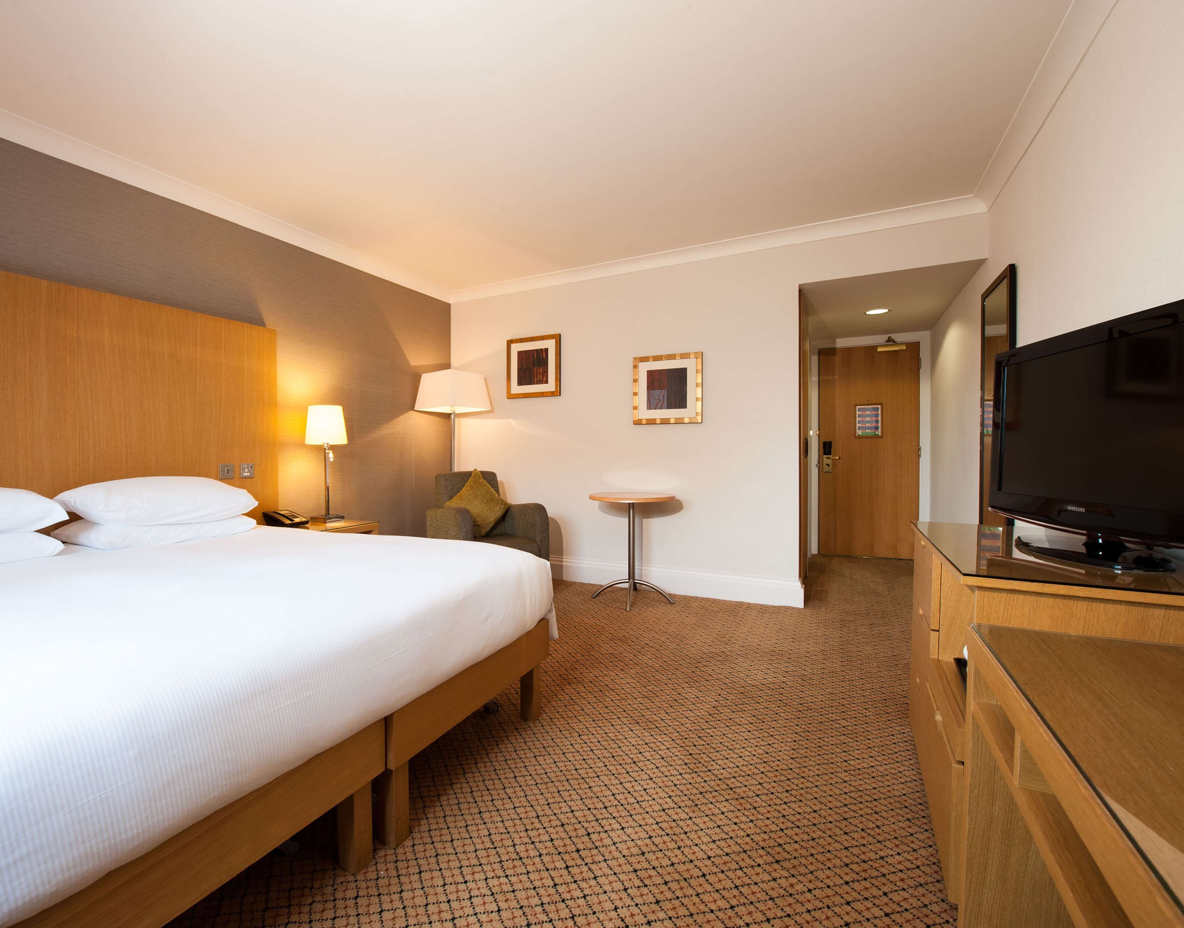 A hotel room with a bed, a chair, a desk, a television, and a door leading to another room.
