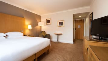 A hotel room with a bed, a chair, a desk, a television, and a door leading to another room.