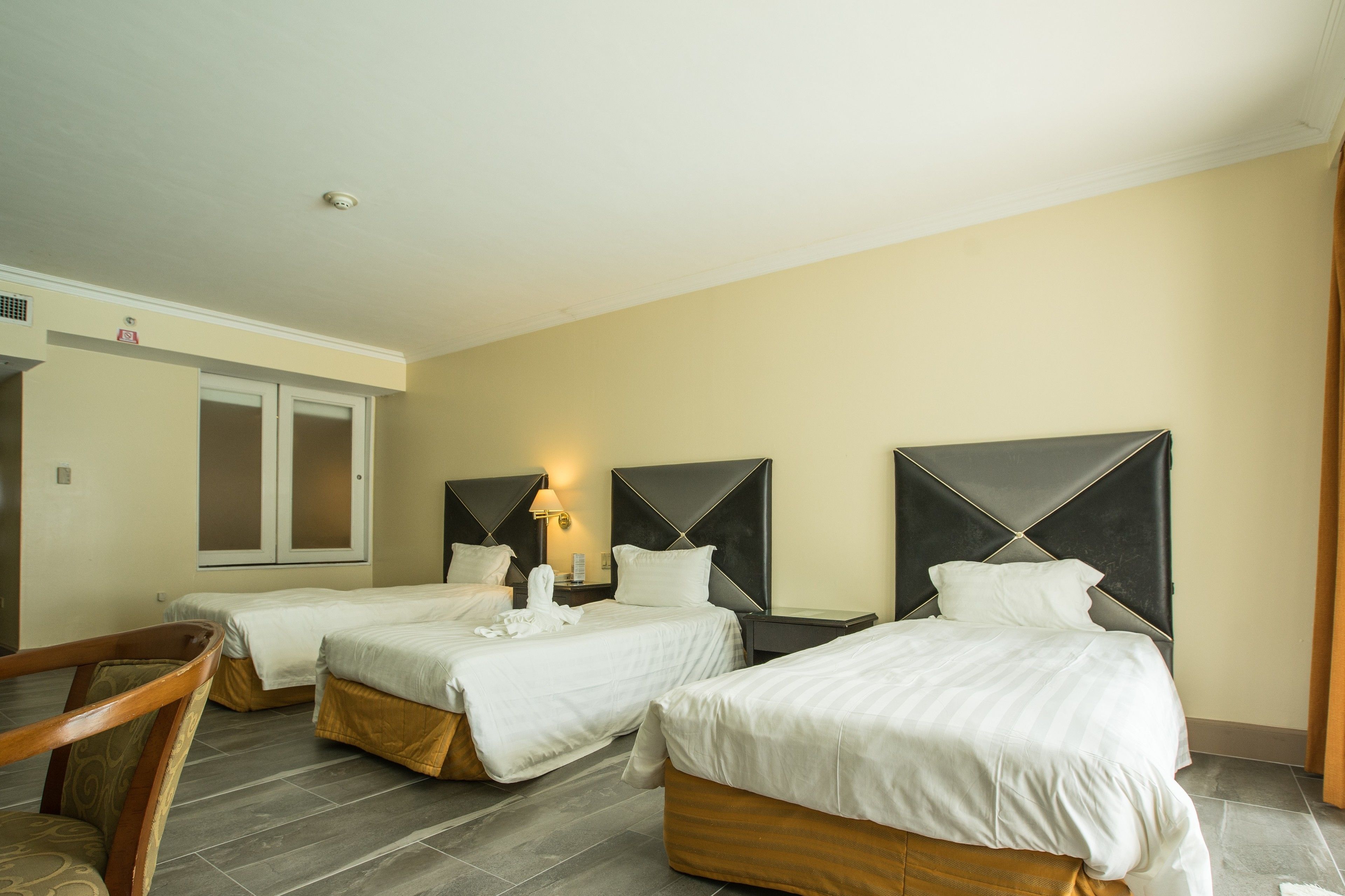 A hotel room with three single beds, a wooden chair, and a small table.