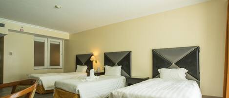 Una habitación de hotel con tres camas individuales, una silla de madera y una mesita.
