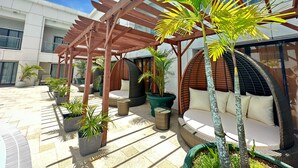 Un patio al aire libre con una pérgola de madera, zonas de estar y plantas en macetas.