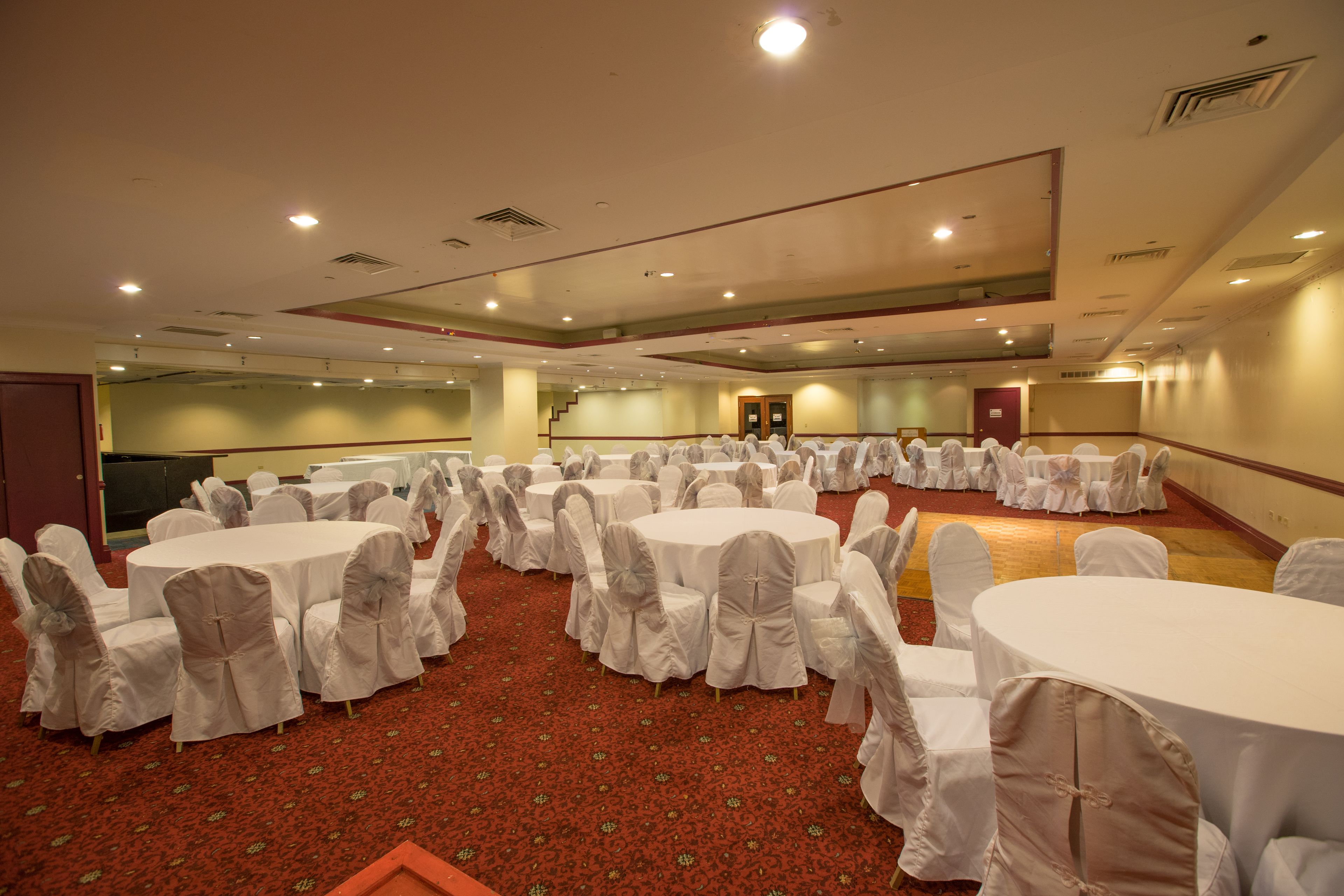 A large conference room with multiple round tables and chairs, carpeted floor, and recessed lighting.