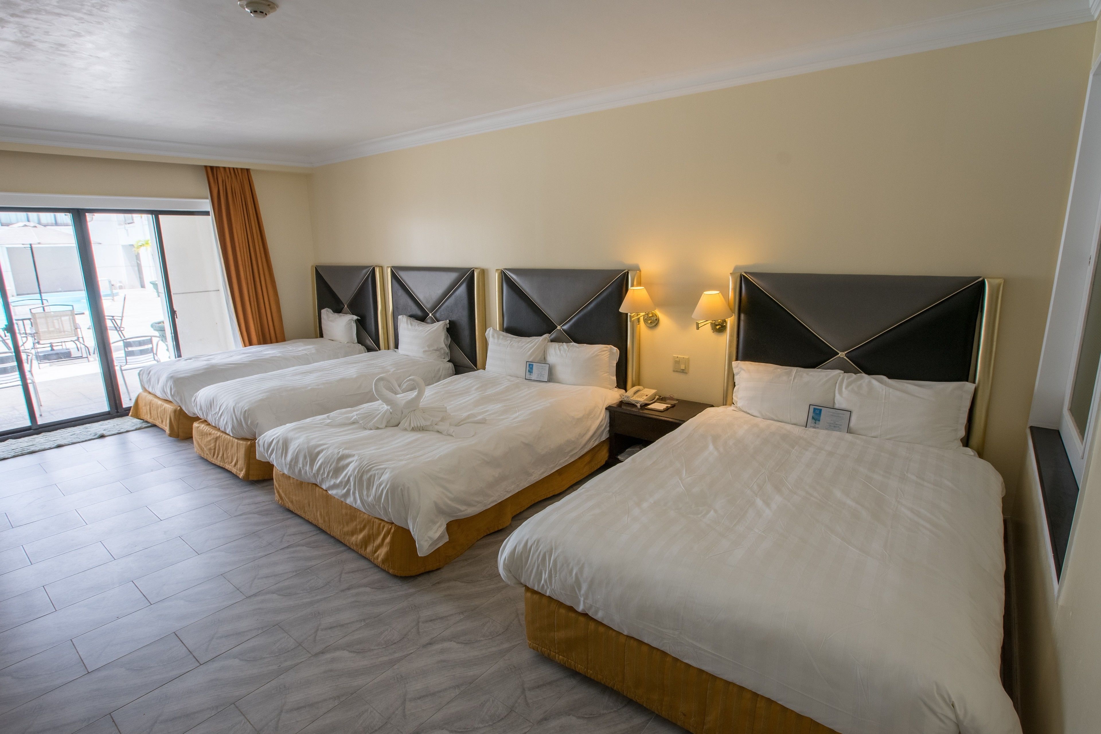 A hotel room with three beds, a large sliding glass door, and a view of the outdoors.