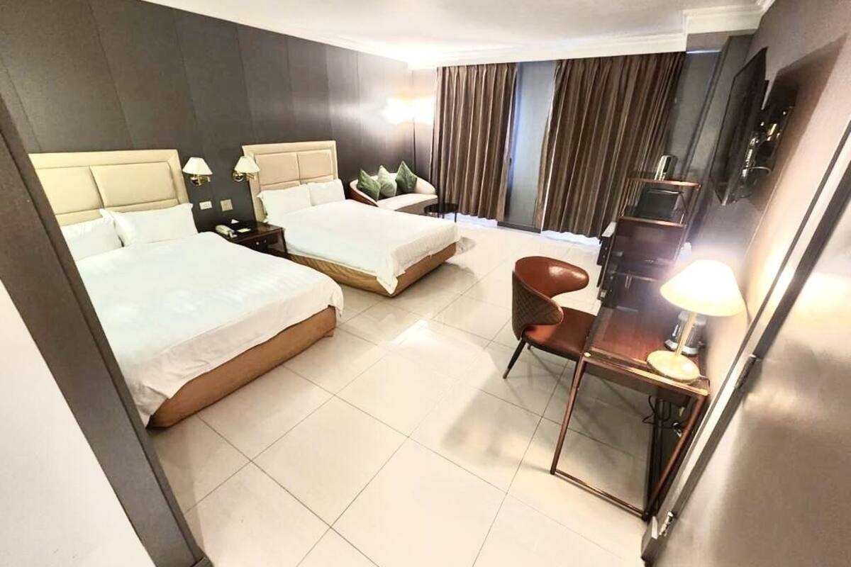 A hotel room with two beds, a desk, a chair, a TV, and a window with curtains.
