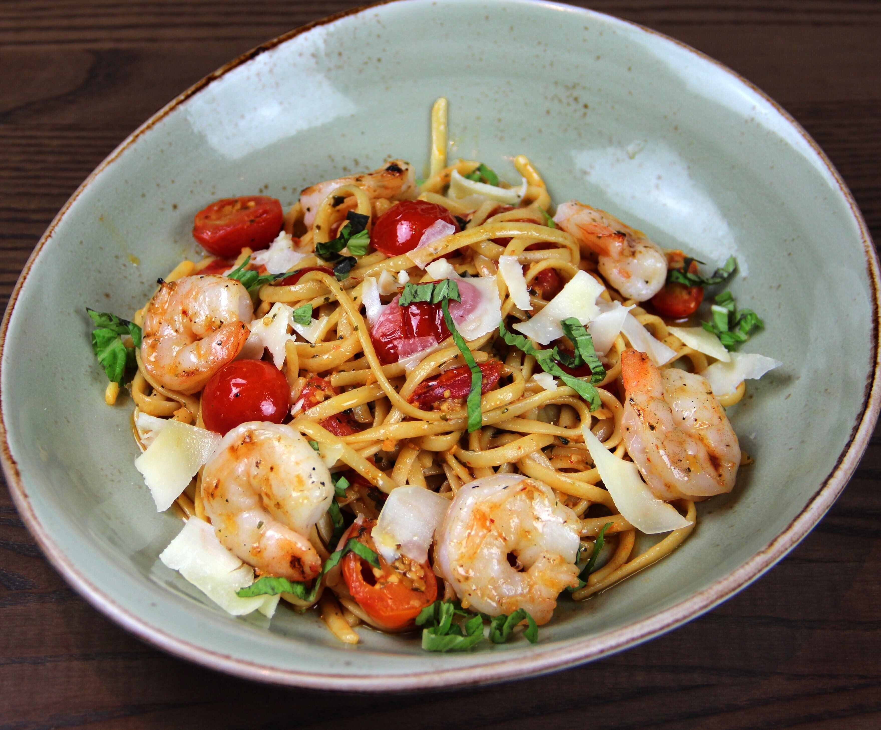 A bowl of spaghetti with shrimp, cherry tomatoes, and herbs.