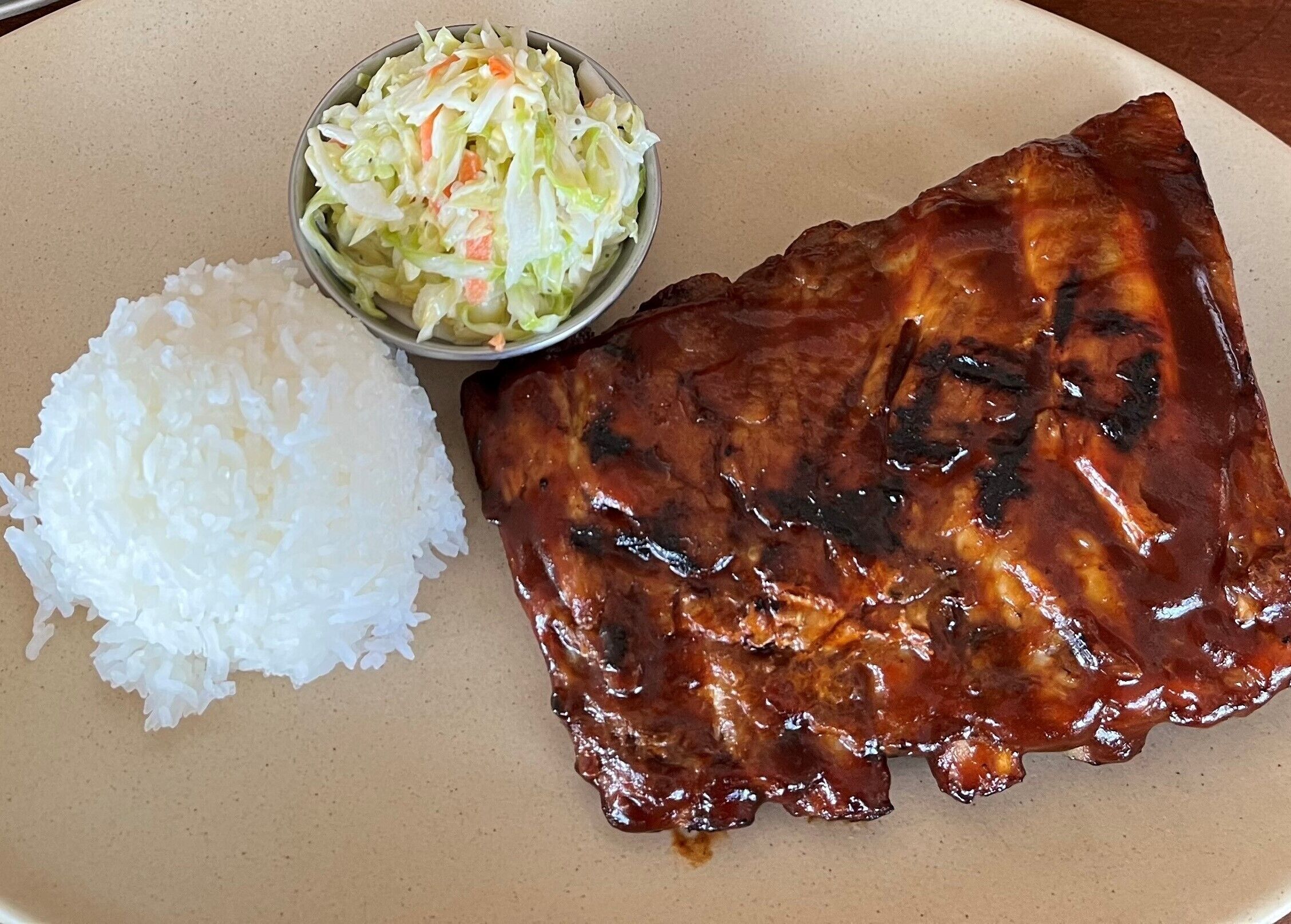 A plate with a piece of grilled meat, a side of white rice, and a coleslaw salad.