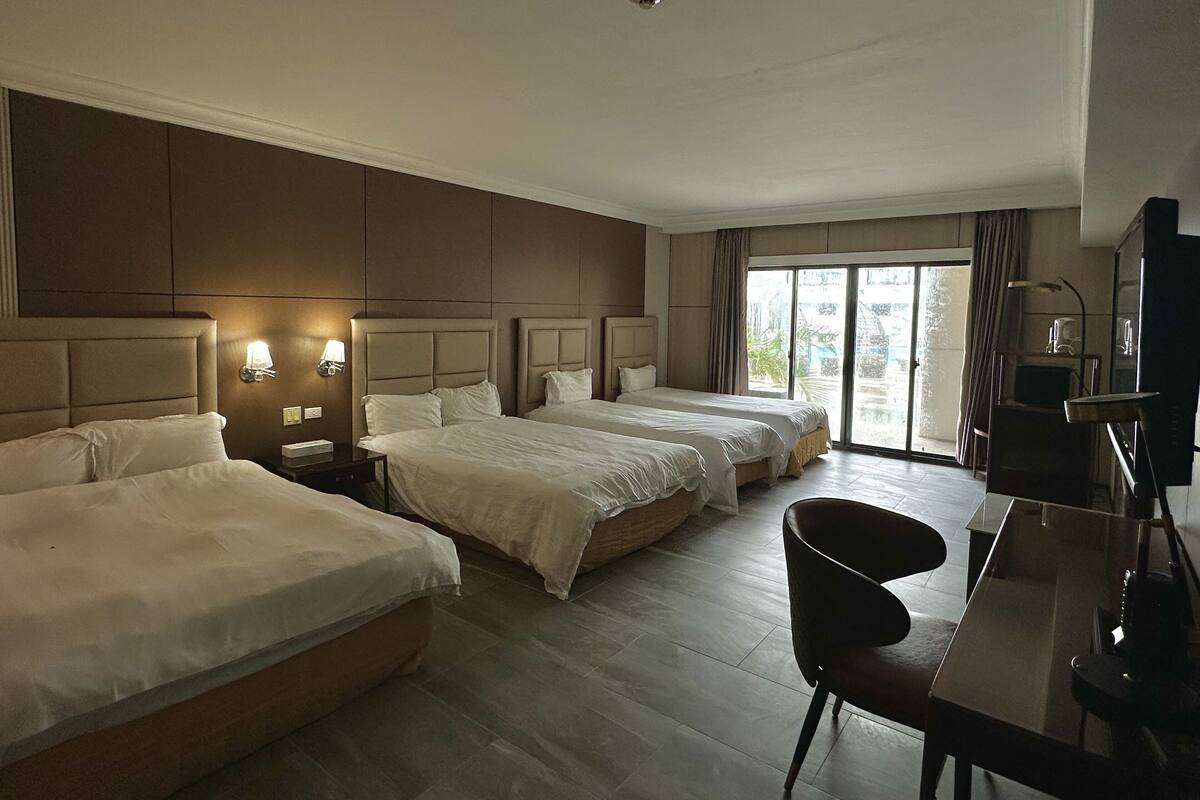 A hotel room with three beds, a desk, and a chair.