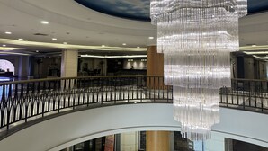Un amplio atrio con una gran y ornamentada araña colgando del techo, barandilla de balcón curva y una zona de recepción al fondo.