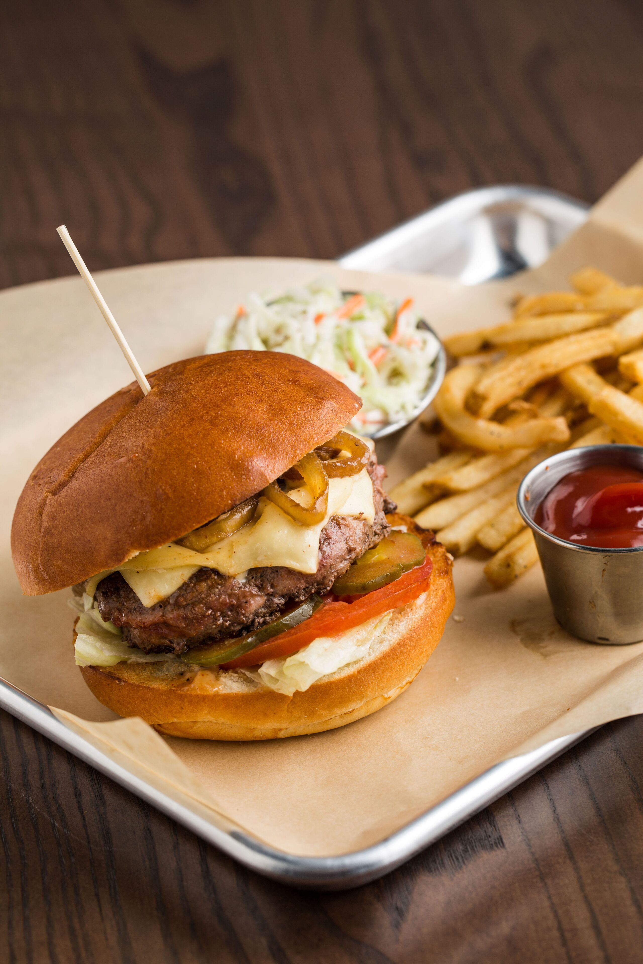 A burger with a toothpick, fries, and a side of coleslaw on a tray.