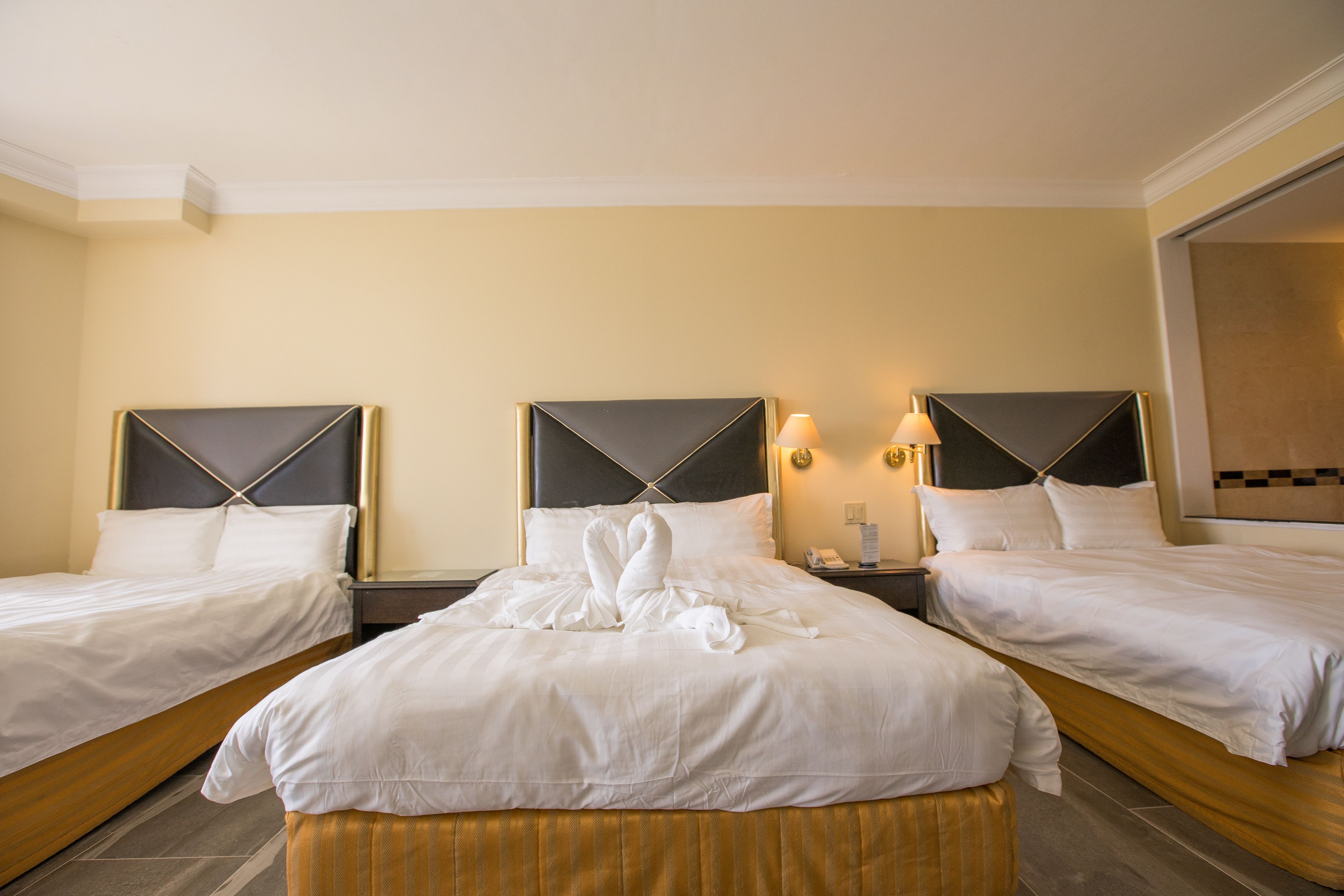 A hotel room with two single beds, a large bed with a swan-shaped bedspread, and a small table between the beds.